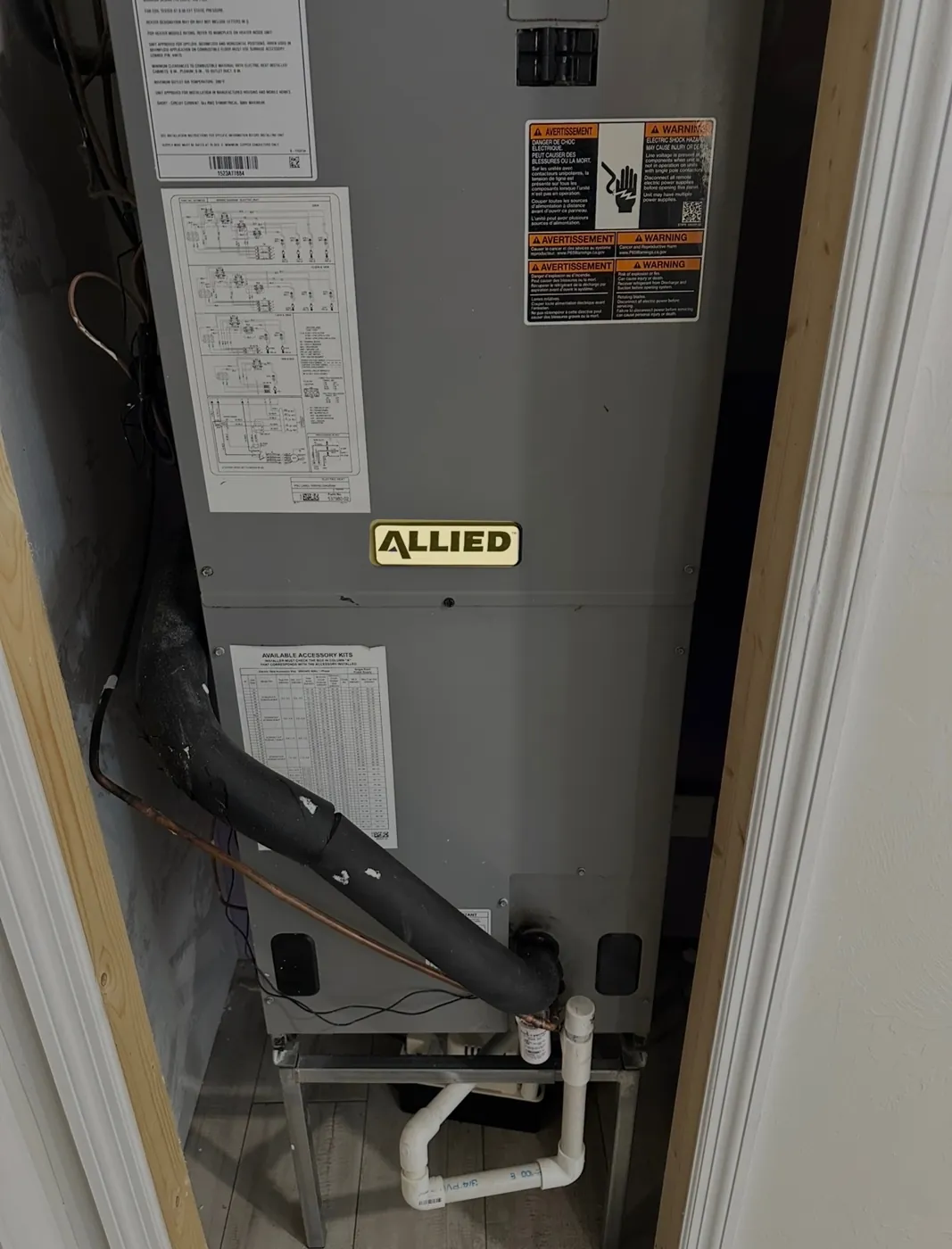 An air handler standing in a closet with refrigerant lines and a condensate drain plumbed at its base