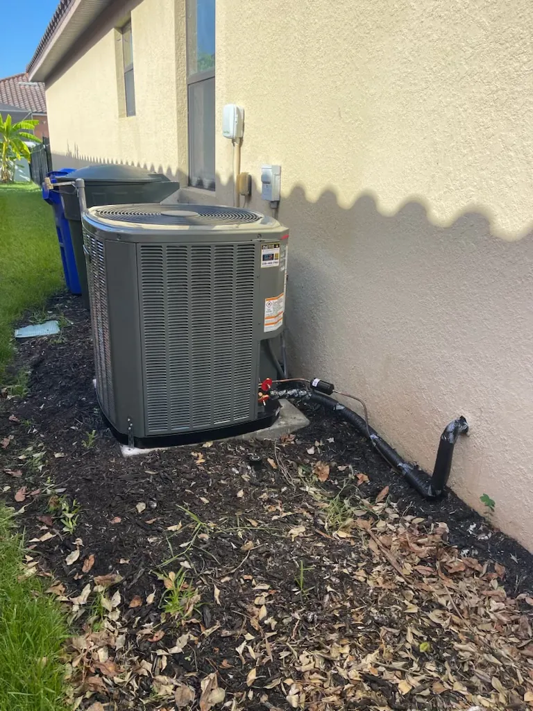 A newly installed condenser on a fresh pad beside a house with the line set run to the wall