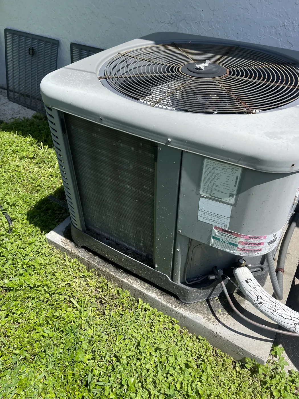 An aging condenser with its coil face matted in dirt and debris